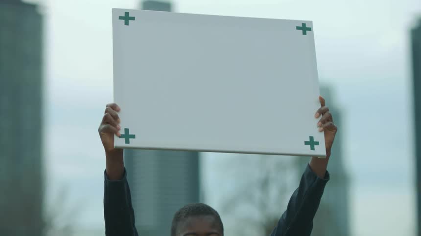 A woman smiles as she raises a sign with symbols on it