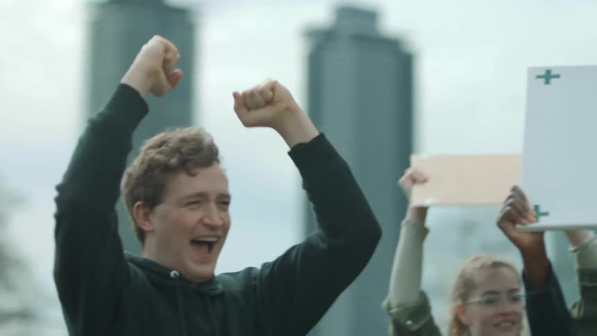 People holding banners protest in the street with high rise buildings in the background