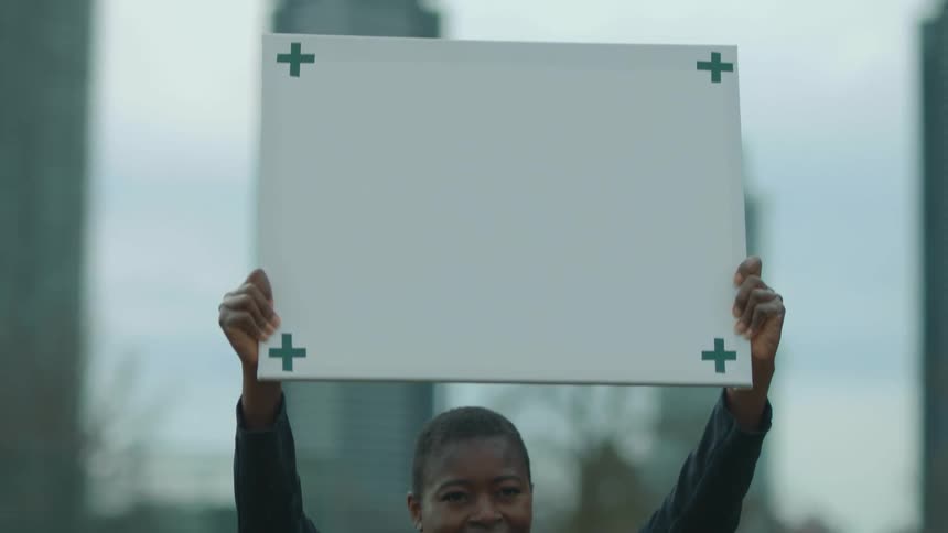 A woman smiles as she lifts a sign