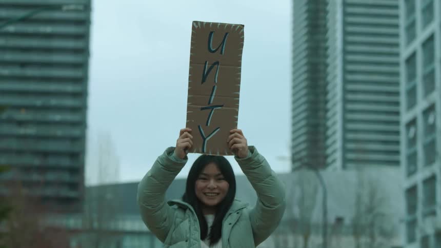 An asian female protester smiles as she holds up her sign in a city