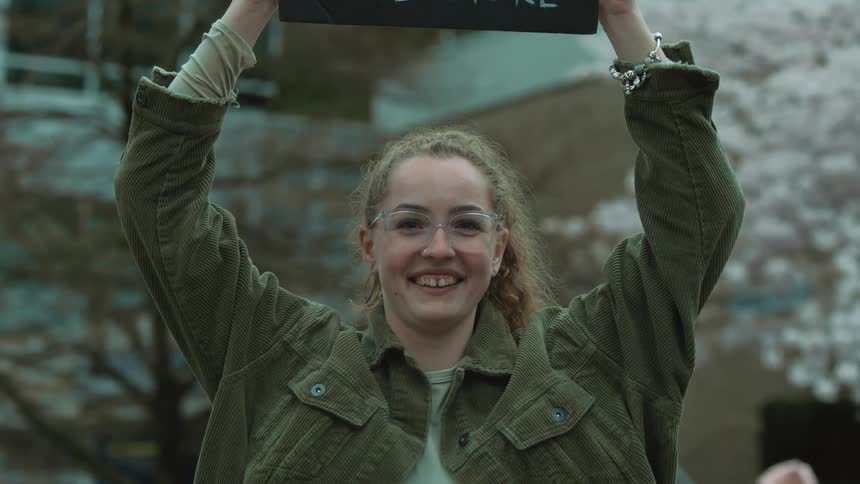 Happy young woman standing outdoors lifting a placard