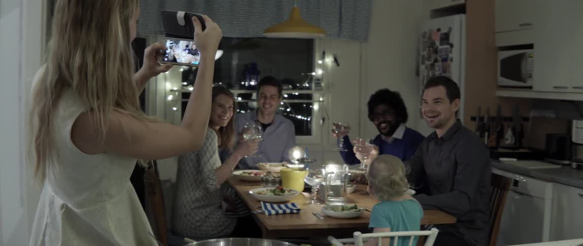 A woman photographs a group of people gathered around a dining room table