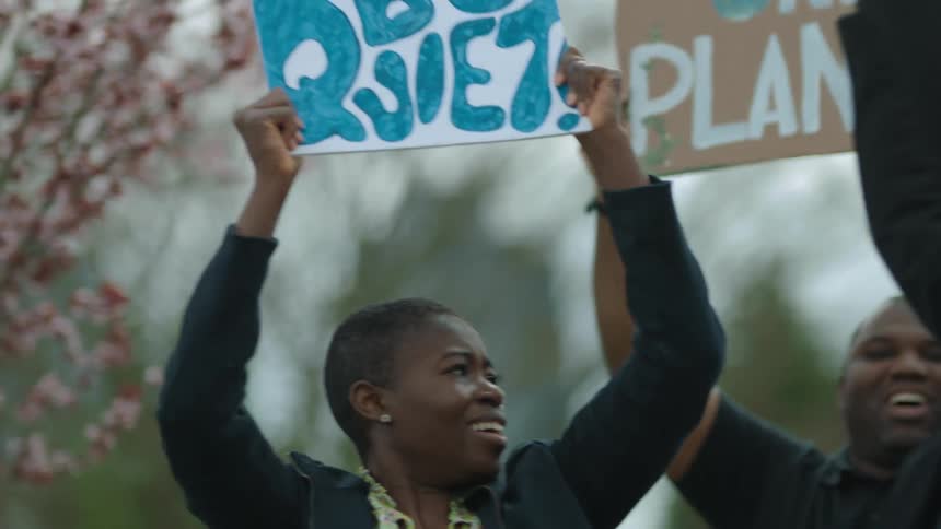A woman holds a sign over her head as she marches with a group of protesters during the day