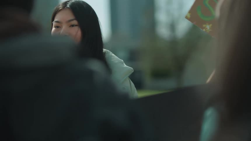 Young asian woman holding a protest sign and using a megaphone to talk to the protest crowd in a public space