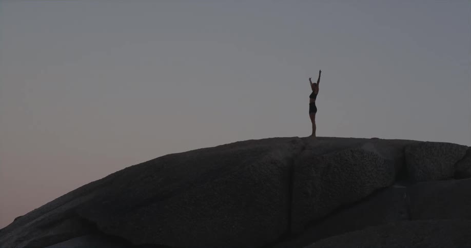 Woman standing on top of a large rock stretching her arms up in the air