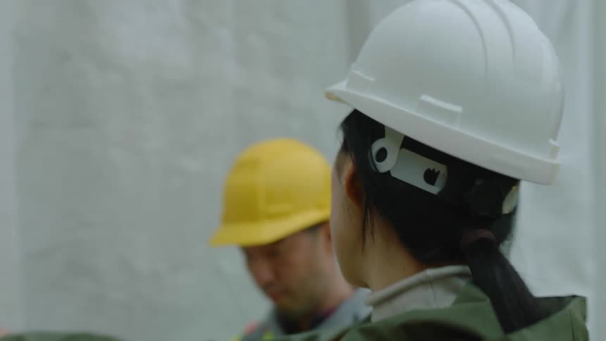 An asian woman wearing a white hardhat is talking to a construction crew as they walk through the construction site