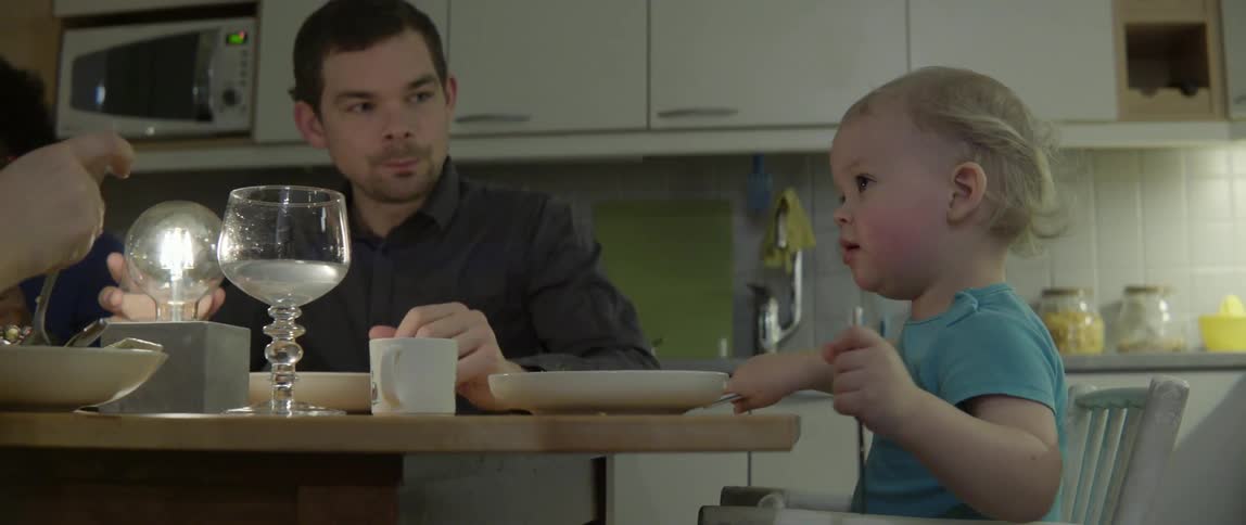 Happy toddler playing with silver utensils during a cozy evening dinner with family members.