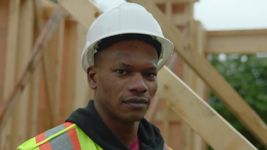 A male construction worker wearing a white hardhat is standing at the construction site