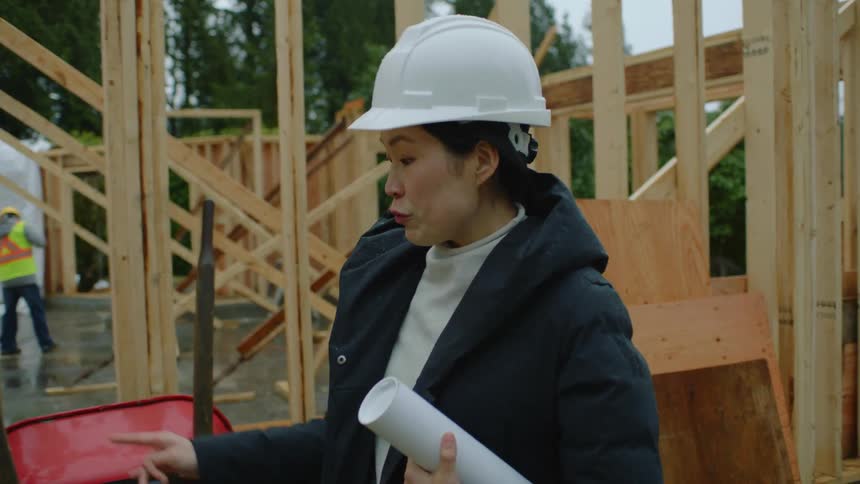 A woman stands on a construction site and talks with one of the construction workers