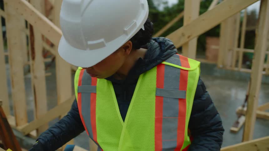 A female construction worker is looking down and marking a board