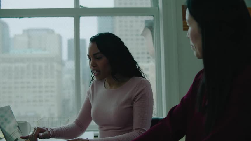 Two women sit in an office and talk as they look at a laptop