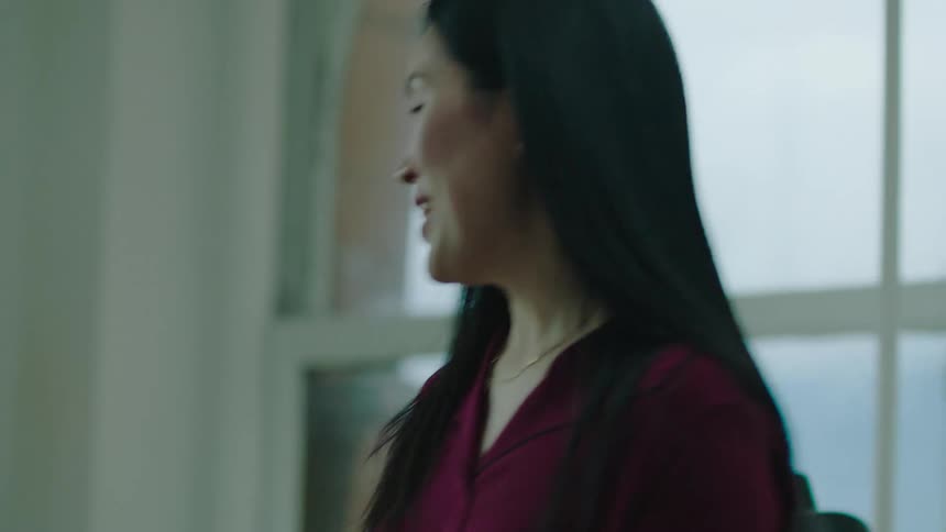 Workers greet arriving woman as they sit in meeting room with window showing city buildings