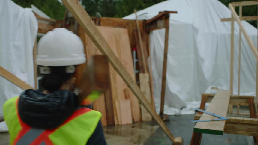 A female construction worker is carrying a piece of wood through a construction site