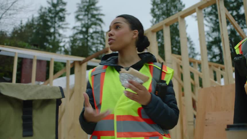 Construction workers are taking a lunch break and a woman is speaking to the crew