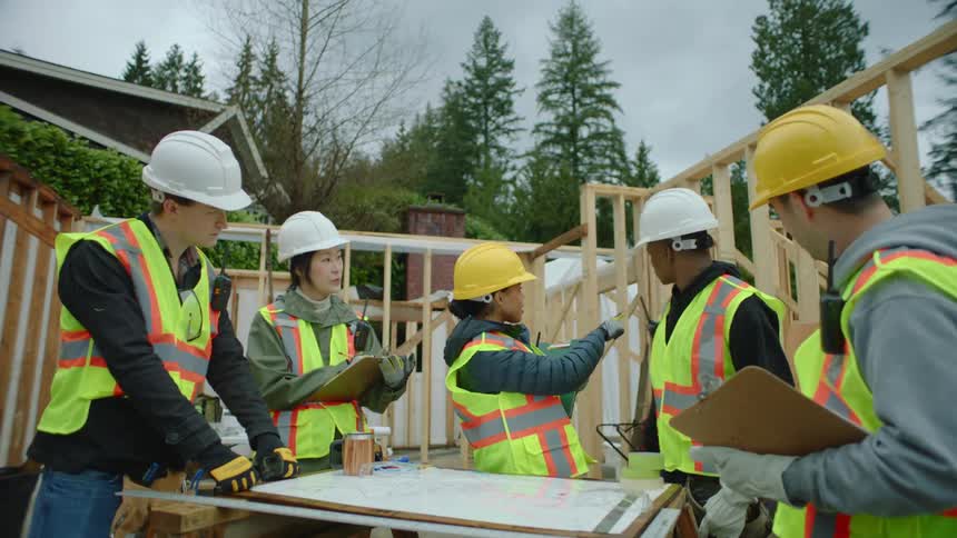 Construction workers are on site standing over a table and a woman is giving them instructions