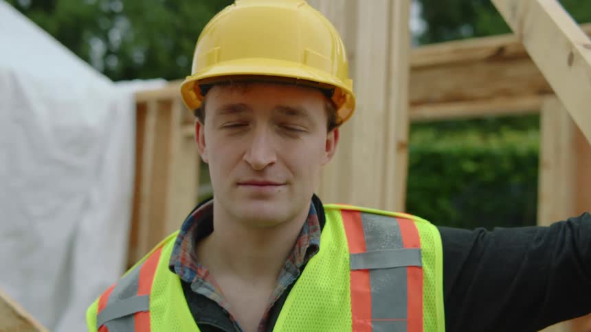 A male construction worker wearing a yellow hardhat is standing at the construction site