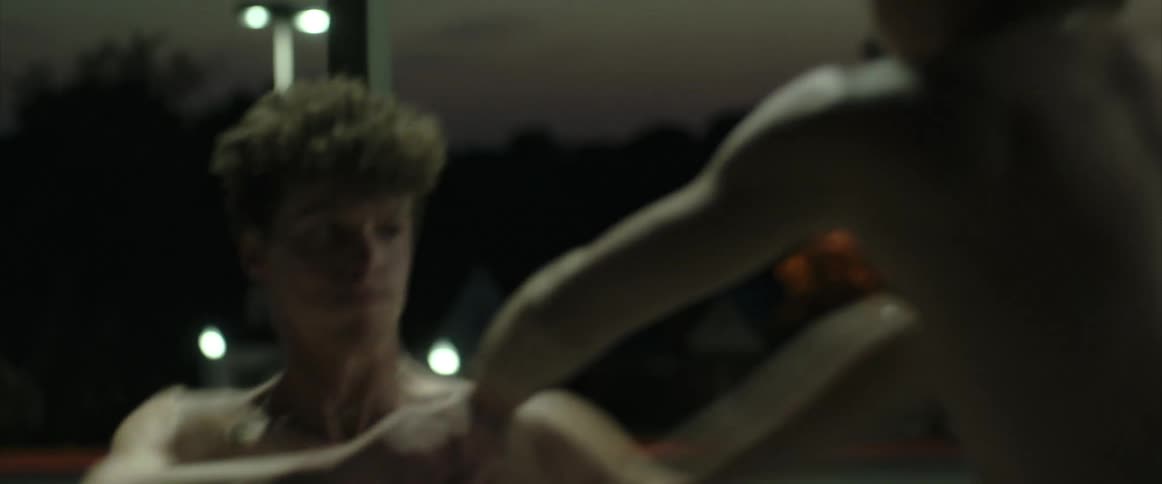 Two shirtless young men fighting in a public space at night with punches and pushes