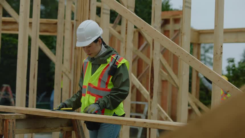 A female construction worker is making measurements on wood at the work site