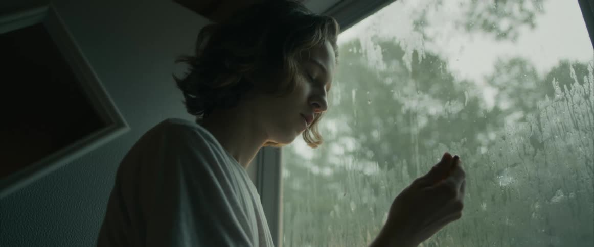 An angry, teenager holding bullet inside by rainy window