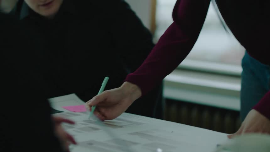 A woman instructs other coworkers with a blue print in an office setting