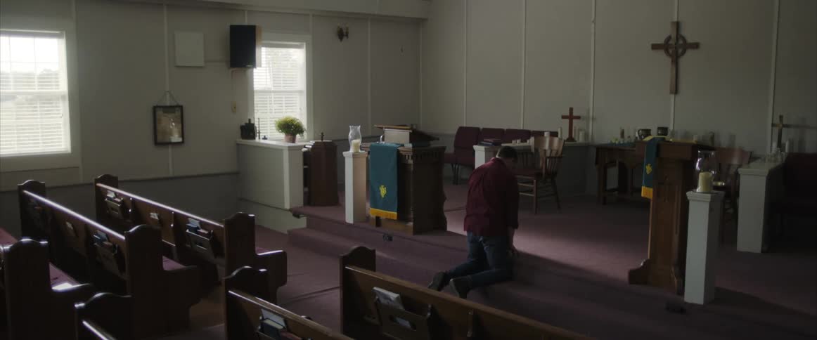 A man is kneeling and praying at the alter of a church alone