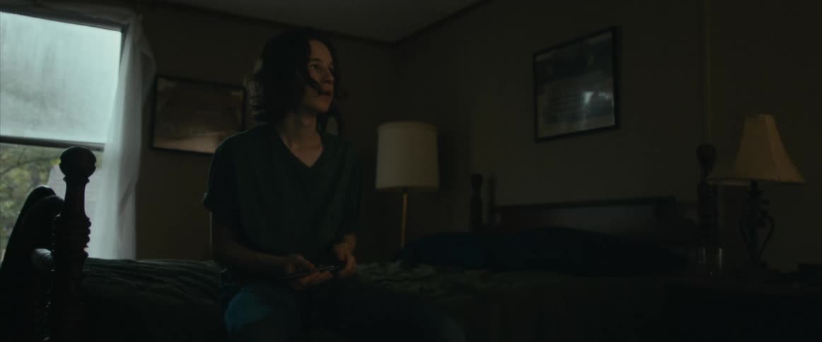 Distressed woman sitting on the bed and holding a handgun in a dark room