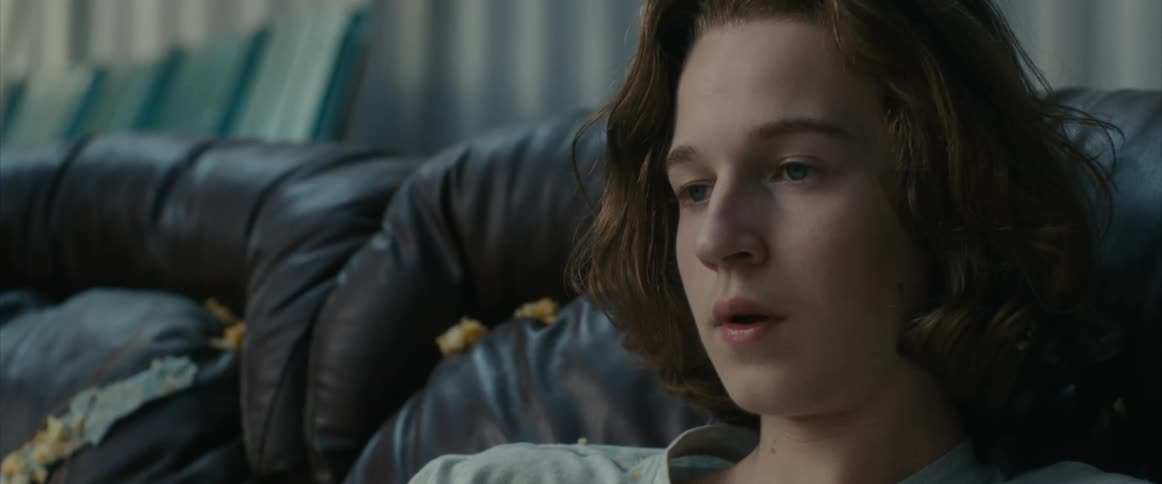 Sad teenage boy with long hair sits on couch outside