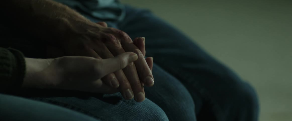 A man and woman are holding hands as they sit in a room