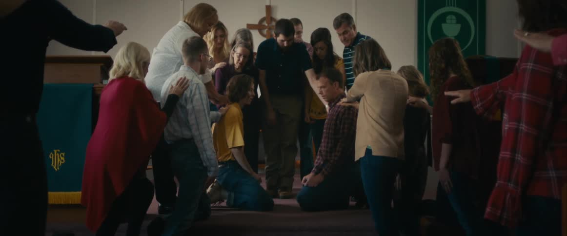 A crowd of people kneel and pray around a man in church