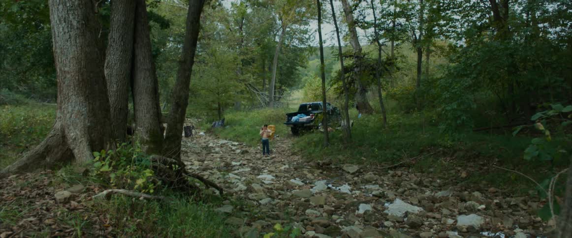 A man stands in behind a truck parked in a forest