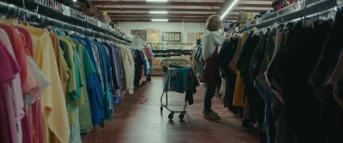 A male store employee hangs clothing on to a thrift store rack