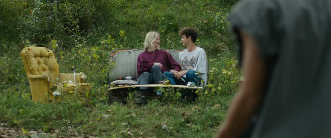 Two teenagers hang out on abandoned furniture watching their friends shoot guns