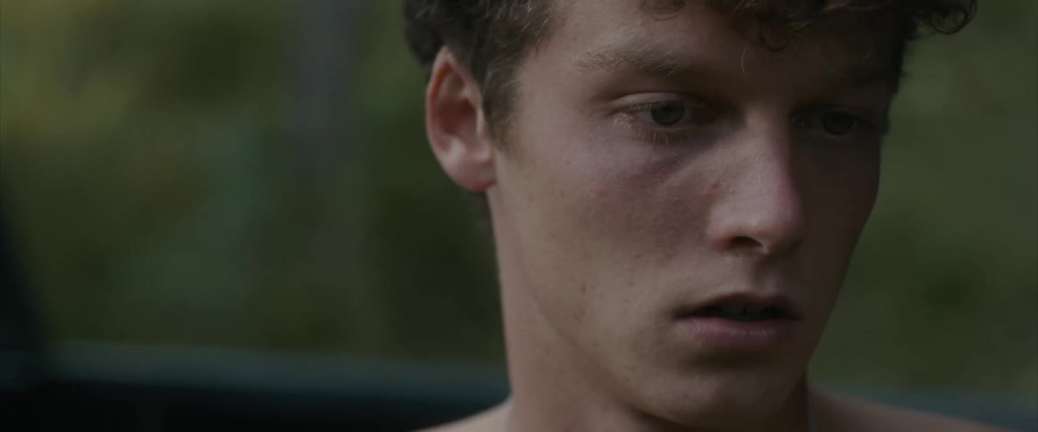 Shirtless teen boy with an anguished look sitting on the pickup truck bed outdoors