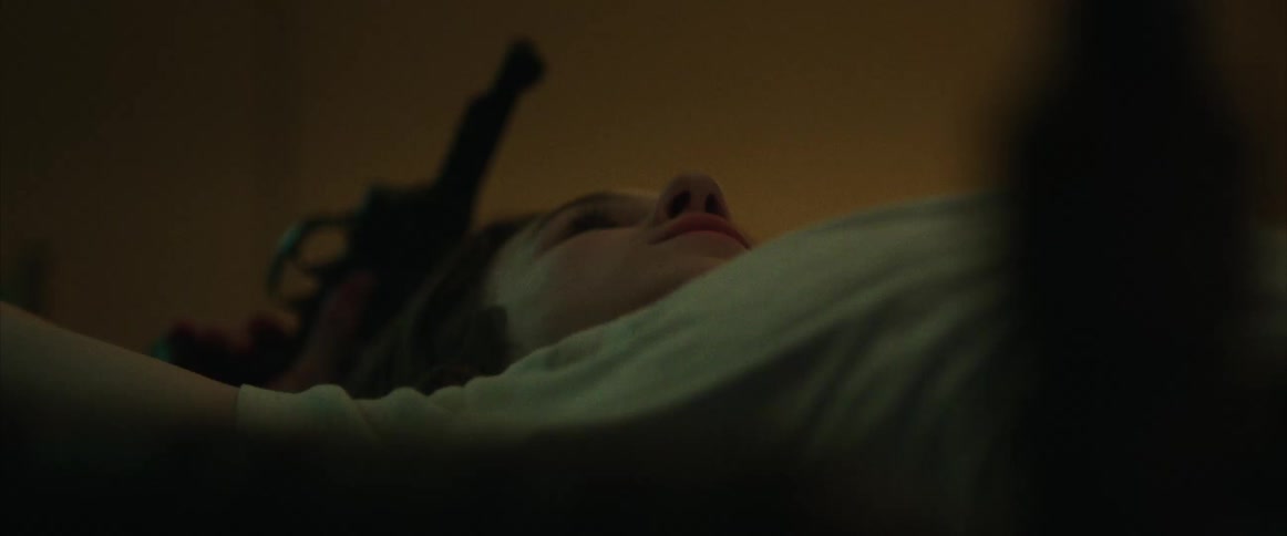 A low angle shot of a teenage boy lying on a bed holding hand gun
