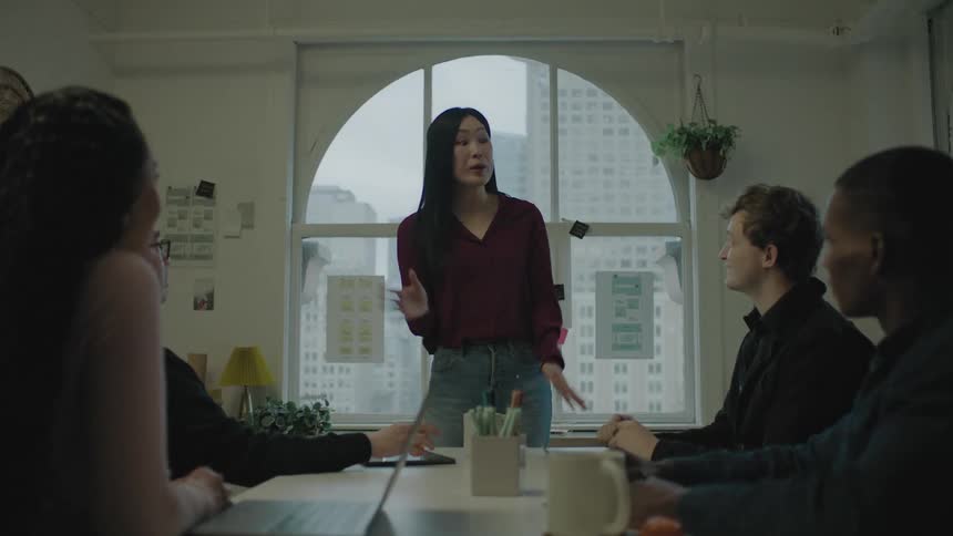 A woman standing at the end of a conference table talks and gestures animatedly then they all clap