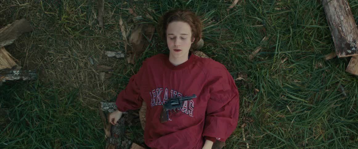 Young man sleeping on the grass outdoors with a handgun in his chest