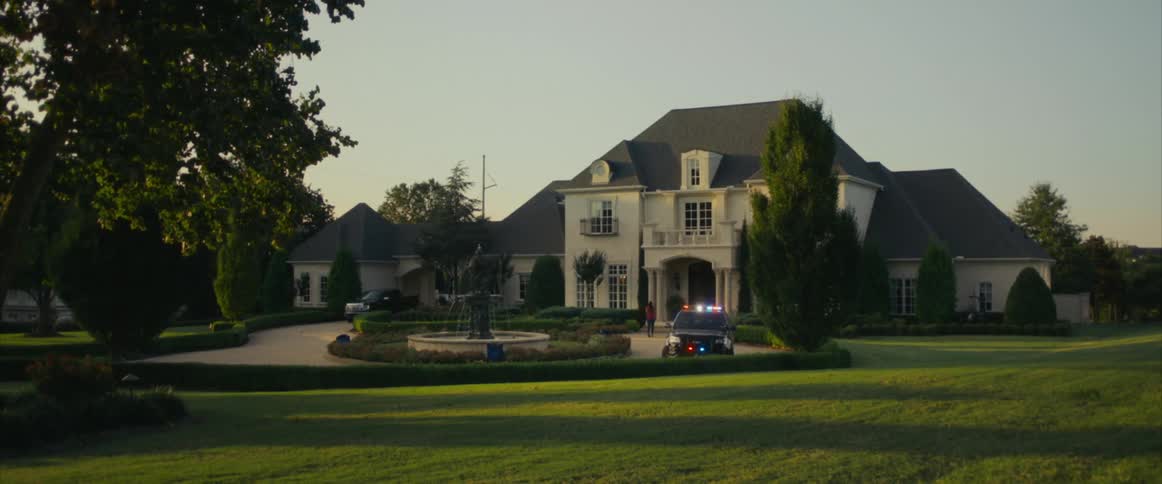 Police vehicle with flashing lights drives down driveway at mansion