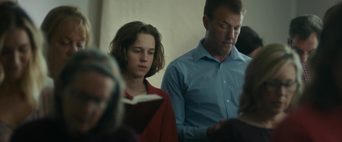 A teenager looks depressed as he stands in a church with his dad and other people