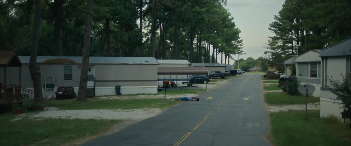 A person is laying on the ground and not moving in a trailer park