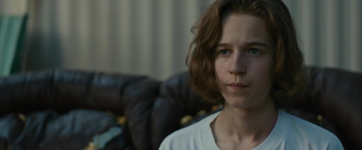 A depressed teenager sitting on outdoor couch looking ahead