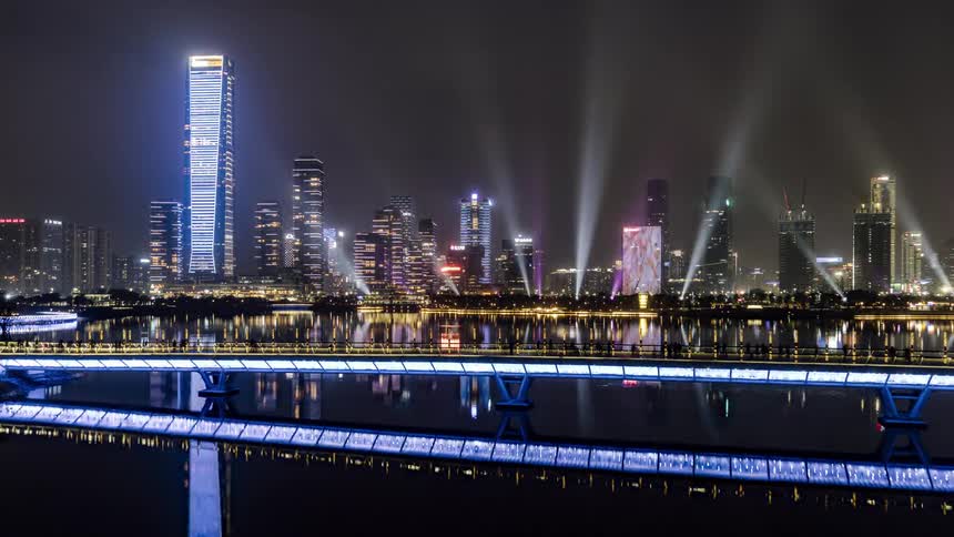 A time lapse of people walking across a bridge with lit up skyscraper in the city skyline