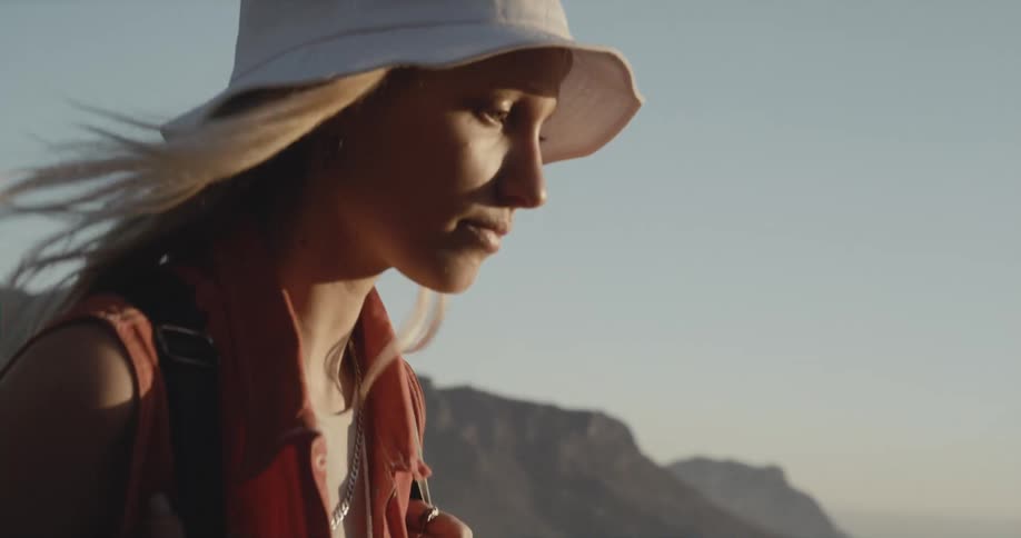 Blonde woman with white hat and black backpack hikes on mountain