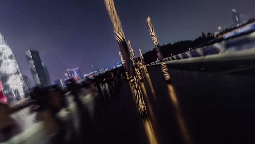 Pedestrians move along reflective path lit by light columns with skyline in distance