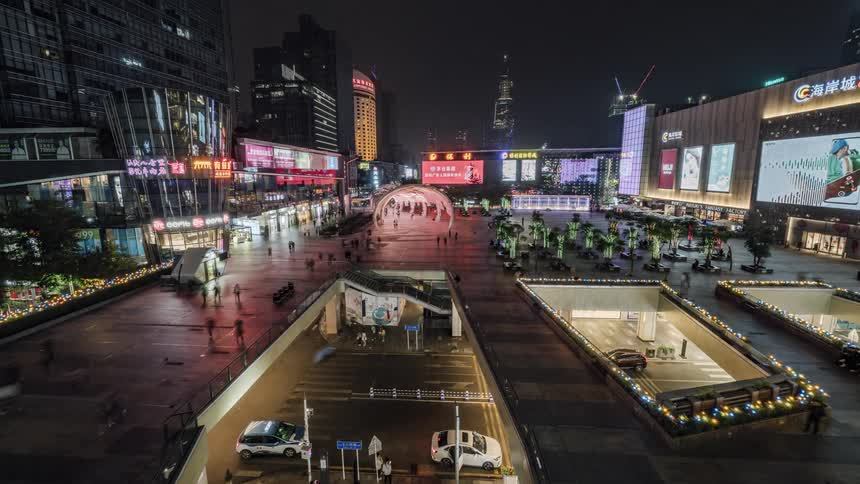 People walking on a pedestrian upper level to malls and shops with cars and people on the street below