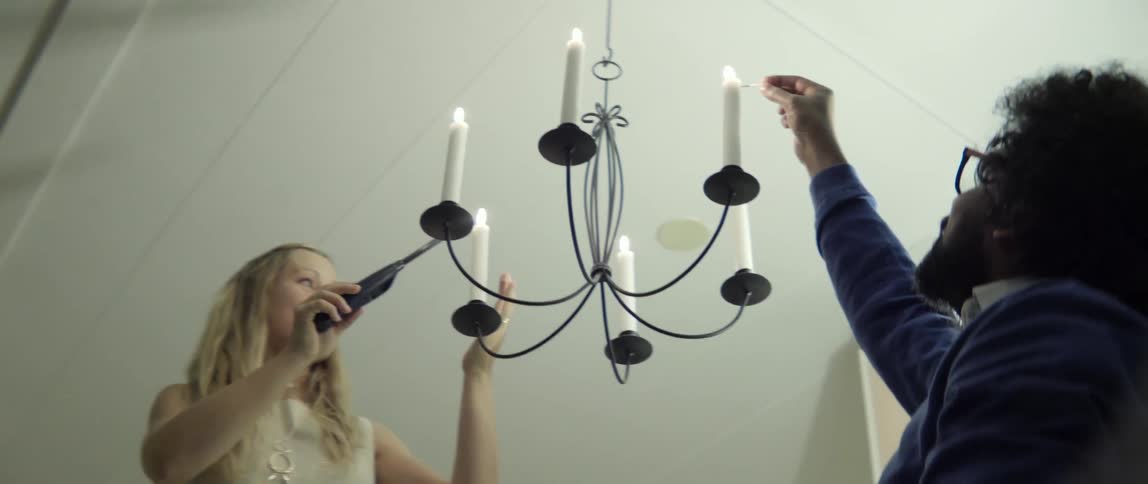 A woman and man light a candelabra that is hanging from the ceiling