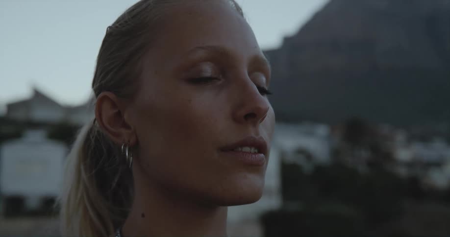 Blonde woman with ponytail and earrings opens her eyes outdoors