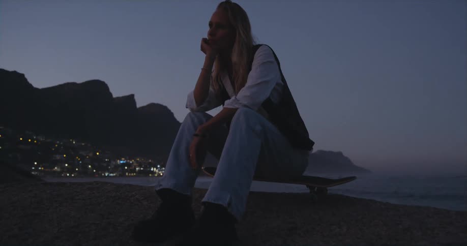 A woman sits on a skateboard on the beach