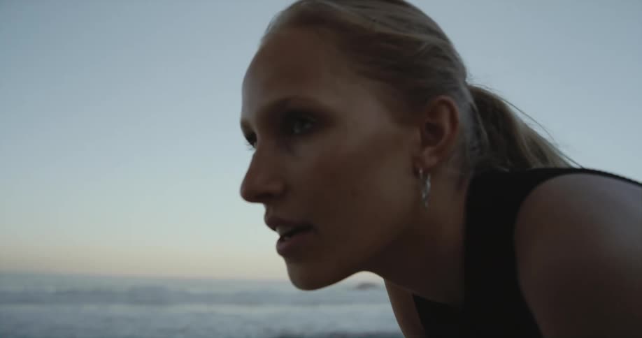 A younger woman is exercising outside by the beach