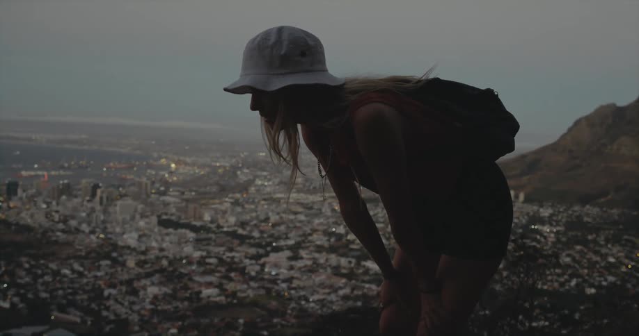 A woman stops on a hike on a ridge with views of a vast neighborhood along the coast