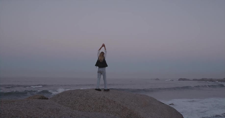 Woman is standing on a rock with the view of the ocean